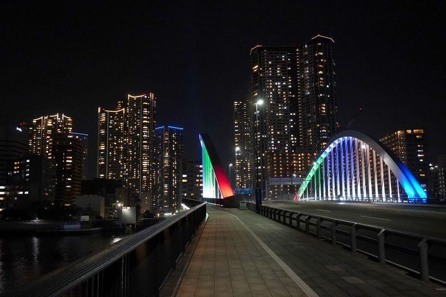 アーチが五色に照らされる築地大橋 ミラノ・コルティナオリンピックにあわせた隅田川橋梁のライトアップ